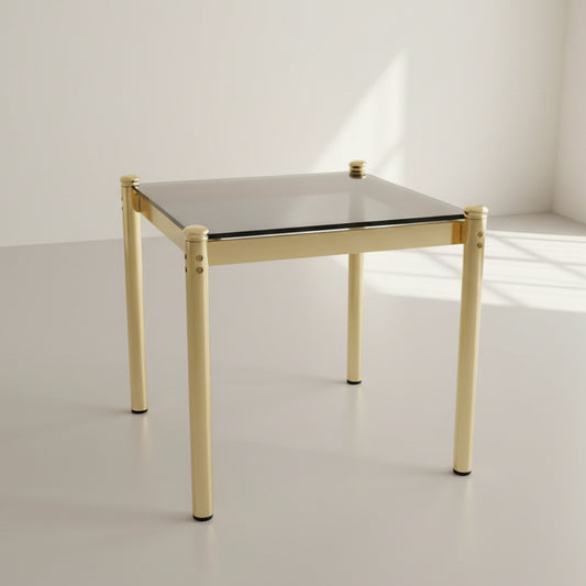 Table with gold legs and black glass top, covered with plastic wrap, on a stone floor.